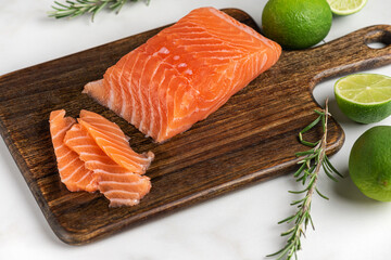 Fresh raw salmon fish fillet with rosemary and lime on wooden cutting board on white marble background. Healthy food