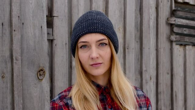 young lumberjack girl in a plaid shirt at the sawmill looks at the camera. Girl in a men's shirt and hat