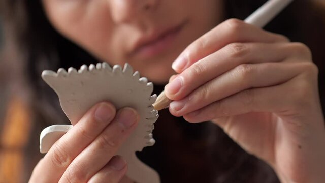 Close up portrait of Pretty asian potter woman working on details of a clay handcraft piece. Work with different pottery tools. Concept of creative ceramics. Start up business, artwork and interior