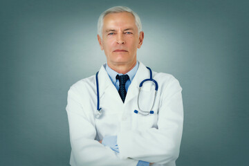 Portrait shot of serious faced male doctor standing with arms crossed at isolated background