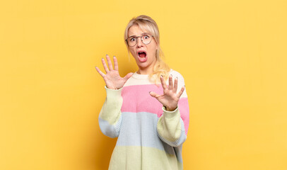 blonde woman feeling terrified, backing off and screaming in horror and panic, reacting to a...
