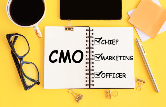 CMO - Chief Marketing Officer acronym, with text on notepad and office accessories on yellow desk.