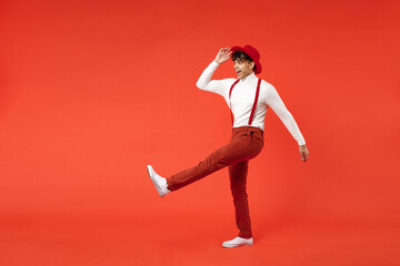 Full length of young spanish latinos surprised stylish fashionable man 20s wearing white shirt trousers touch hat tip, raised up leg with long stride big isolated on red background studio portrait.