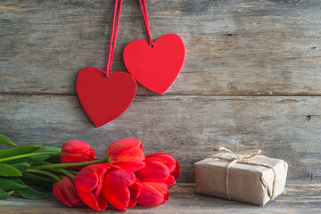Valentine card. Bunch of red tulips, handmade gift box and two red hearts on old non paint wooden...