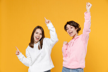 Funny two young women friends 20s wearing casual basic white pink hoodies dancing doing winner...