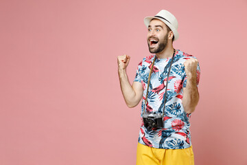 Excited traveler tourist man in hat photo camera doing winner gesture celebrating clenching fists say yes isolated on pink background. Passenger travel abroad on weekends. Air flight journey concept.