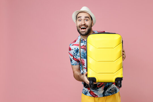 Excited young traveler tourist man in summer casual clothes hat hold suitcase isolated on pink background studio portrait. Passenger traveling abroad on weekends getaway. Air flight journey concept.