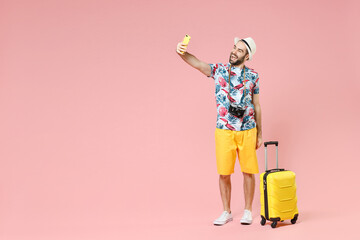 Full length of laughing young traveler tourist man in summer clothes hat doing selfie shot on mobile phone isolated on pink background. Passenger traveling on weekends. Air flight journey concept.