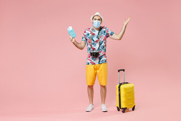 Full length irritated traveler tourist man in mask to safe from coronavirus hold passport tickets spreading hands isolated on pink background. Passenger travel on weekends. Air flight journey concept.