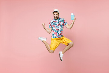 Fototapeta na wymiar Full length happy traveler tourist man in summer clothes hat jumping hold passport tickets doing winner gesture isolated on pink background. Passenger traveling on weekend. Air flight journey concept.