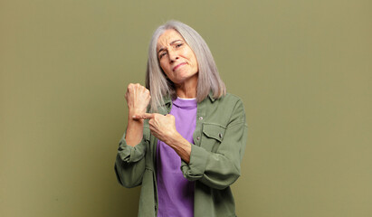 senior woman looking impatient and angry, pointing at watch, asking for punctuality, wants to be on...