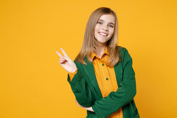 Little blonde happy smiling kid girl 12-13 years old wearing casual clothes green shirt show victory v-sign gesture isolated on yellow background children studio portrait. Childhood lifestyle concept.