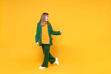 Full length little blonde smiling kid girl 12-13 years old in casual clothes point index finger aside on workspace area isolated on yellow background children portrait. Childhood lifestyle concept