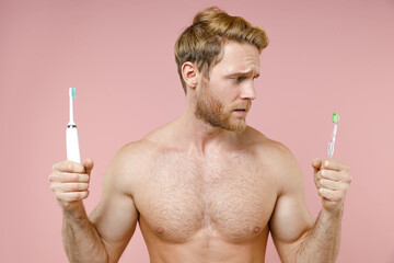 Confused puzzled bearded naked young man 20s years old perfect skin hold choice electric brushes...