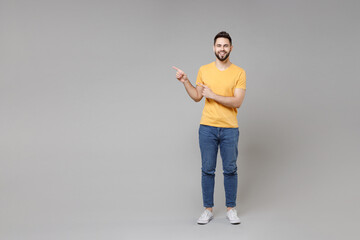 Fototapeta na wymiar Full length young caucasian smiling cheerful bearded attractive happy man in casual yellow basic t-shirt point index finger aside on copy space area isolated on grey color background studio portrait.