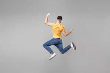 Fototapeta na wymiar Full length back rear view of young bearded cool student frelancer man 20s in yellow basic t-shirt jump high do winner gesture clench fist celebrating isolated on grey background studio portrait