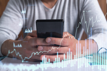 Trader holding in the hands a smart phone and researching stock market to proceed right investment solutions. Internet trading and wealth management concept. Hologram Forex chart over close up shot.