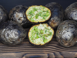 Fried potatoes with skin baked in wood charcoal on the kitchen board, closeup, flat layout. Healthy grilled vegetables with potassium for dietary and vegetarian meals, cooked over a campfire