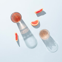 Two glasses of juice with slices of fresh grapefruit on pastel blue background. Creative minimal summer aesthetic. Sunny day shadows.