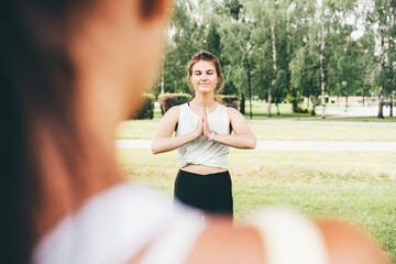 Tranquil athletic women in sportswear do yoga exercises standing on lush green grass under railway...