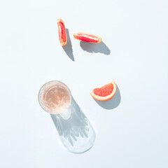 A glass of juice with slices of  fresh grapefruit on pastel blue background. Minimal summer aesthetic.