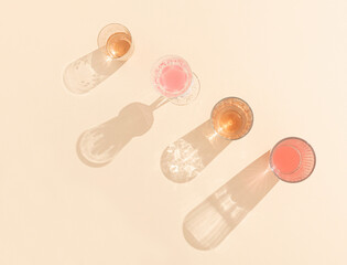 Glasses of colorful drinks with sunlit shadows on bright beige background. Creative summer party concept. Top view.