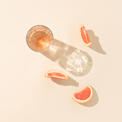 A glass of drink with slices of fresh grapefruit on a bright beige background. Minimal summer aesthetic. Sunny day shadows.
