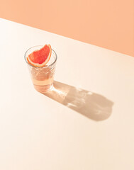 A glass of drink with a slice of fresh grapefruit against bright beige and orange background. Creative minimal summer concept. Sunny day shadow.