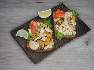 Fototapeta na wymiar Bruschetta, toast with toasted rye bread, mussels, shrimp, pickled ginger, lime and cream cheese on a wooden kitchen board, flat layout. Recipe for a quick light snack with delicious seafood, top view