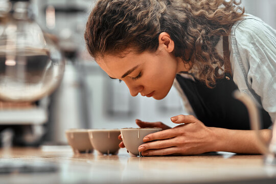 Checking quality. Close up view portrait of a beautiful young woman professional Q Grader test and inspecting the quality of coffee from cup on the table. - Powered by Adobe