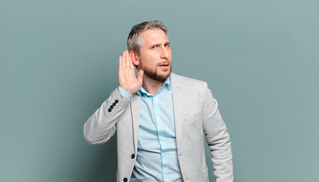 adult businessman looking serious and curious, listening, trying to hear a secret conversation or gossip, eavesdropping