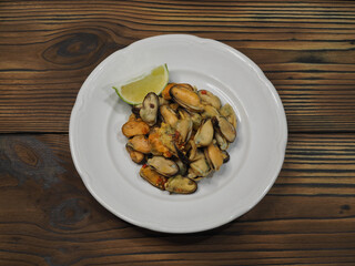 Simple salad with peeled mussels, spices and lime in a white plate on a wooden background, flat layout. Recipe for a quick light snack with delicious seafood for proper and dietary nutrition, top view