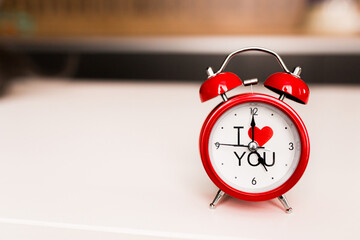 A red alarm clock with a white dial and the inscription I love you, stands on the table. Time to love. Valentine's Day.
