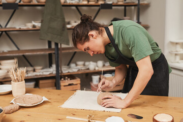 Side view portrait of young man decorating ceramic bowl in pottery workshop, hobby and small business concept, copy space
