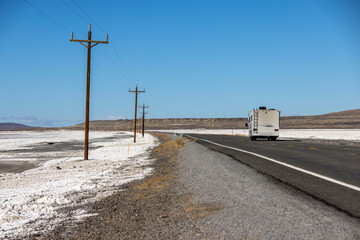 Recreational vehicle traveling down an empty highway stretching for miles into the desert