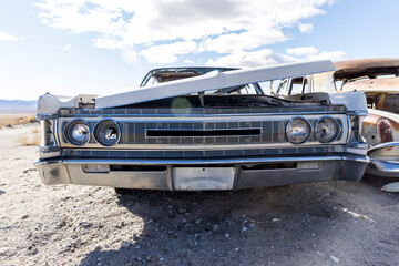 White vintage auto in decent condition sits with hood partially removed in a desert junkyard