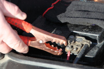 White hand connection the red + clip to car battery pin close up, quick start diesel car engine...