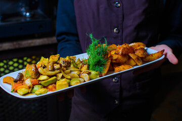 The waiter holds fried vegetables on a wooden board