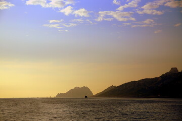 Naklejka na ściany i meble Sunset on the sea with the coast and a ship in backlight