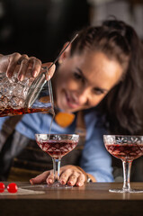 Female bartender pours manhattan cocktail into an ornamental glass