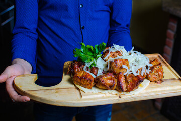 The waiter holds fried meat on a wooden board. Serving barbecue with herbs