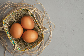 eggs in wicker basket with hay on concrete background or surface, concept of Easter or holiday, place for copy space
