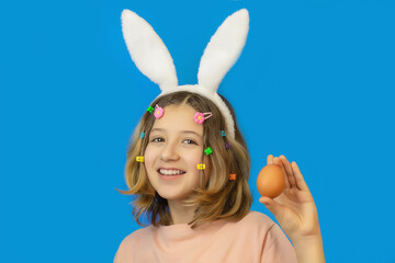 happy girl with bunny ears on her head holds an egg in her hands and congratulates her on the holiday