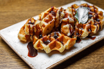 Freshly baked shortbread waffles, drizzled with chocolate, decorated with basil leaves, served on a rectangular plate on a wooden background. Dessert at the restaurant.