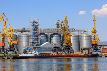 Big port at sea, harbor, pier by the water. Yellow harbor cranes unload a barge at the Odessa seaport among large metal tanks. Unloading of ships, transport, Odesa.