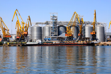 Fototapeta na wymiar Big port at sea, harbor, pier by the water. Yellow harbor cranes unload a barge at the Odessa seaport among large metal tanks. Unloading of ships, transport, Odesa.