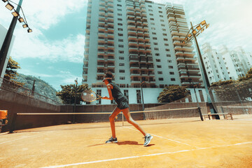 A wide-angle view from behind of a slim sport black female playing a tennis game and hitting the...