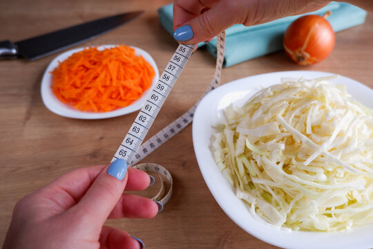 Healthy eating. Measuring tape in female hands, 60cm waist. Raw, chopped vegetables for salad on white plates. Cabbage, carrots, onions.