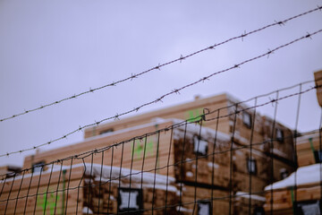 Close-up of barbed wire guarding an industrial area of a woodworking factory, in a gloomy, cold light, in winter