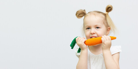 Little girl is eating toy knitt carrots healthy food on the white background